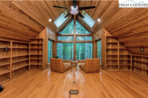 a beautiful room in a home for sale in West Jefferson NC with hardwood floors and ceilings and huge windows overlooking a forest