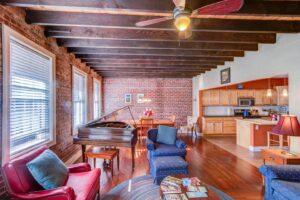 the living room in a home for sale in Ashe County NC, including sofas, a piano, and brick walls
